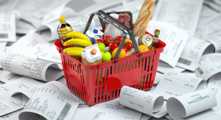 Roter Einkaufskorb mit Lebensmitteln steht auf einem Haufen von langen Kassenbons.
