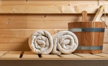 Zwei zusammengerollte Handtücher und ein Saunaeimer liegen bereit in einer Holzsauna.