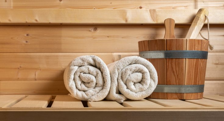 Zwei zusammengerollte Handtücher und ein Saunaeimer liegen bereit in einer Holzsauna.