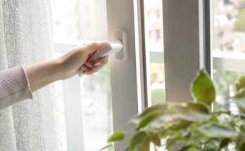 Hand öffnet ein Fenstergriff, um frische Luft hereinzulassen.