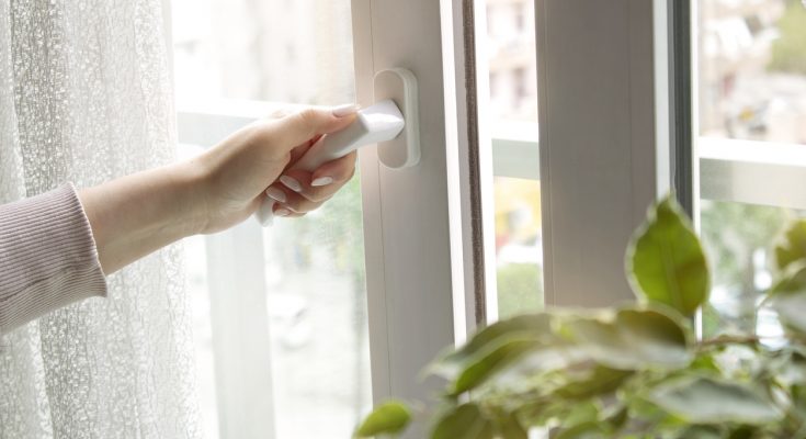 Hand öffnet ein Fenstergriff, um frische Luft hereinzulassen.