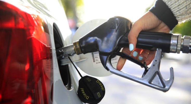 Hand mit Zapfpistole tankt ein Auto an der Zapfsäule.