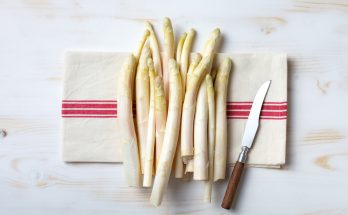 Bund weißer Spargelstangen liegt mit Messer auf einem Geschirrtuch.