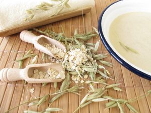 Schale mit Haferflockenbad steht neben Haferflocken, Körnern und einem Handtuch.