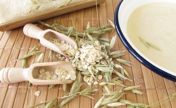 Schale mit Haferflockenbad steht neben Haferflocken, Körnern und einem Handtuch.