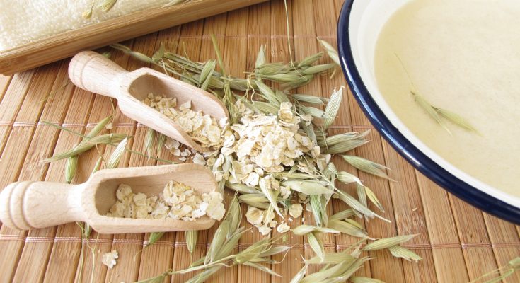 Schale mit Haferflockenbad steht neben Haferflocken, Körnern und einem Handtuch.