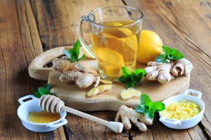 Glas Ingwertee mit Zitronenscheiben, frischem Ingwer, Minze und Honig auf einem Holzbrett.