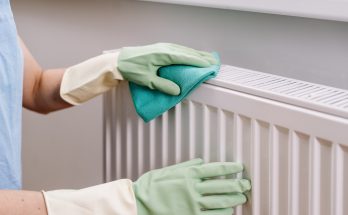 Person mit Gummihandschuhen wischt einen Heizkörper mit Tuch sauber.
