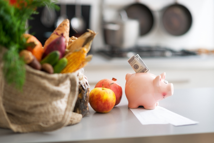 Sparschwein mit Geldscheinen neben Lebensmitteln und Kassenzettel als Symbol für das Sparen beim Einkauf im Supermarkt.